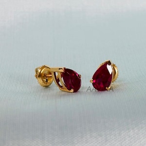 May include: A pair of gold earrings with red pear-shaped gemstones.