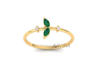 May include: A delicate gold ring featuring a leaf-like design with two marquise-cut emeralds and two small diamonds. The ring has a thin band and is set against a white background. The brand name "AAVIRA" is visible on the ring.