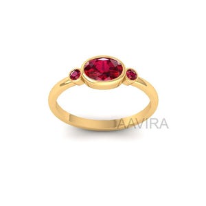 May include: A gold ring featuring a large oval-cut ruby gemstone, flanked by two smaller round rubies. The ring has a simple, elegant design with a polished finish. The ring is a size 7.
