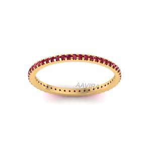 May include: A gold band ring with a row of small red gemstones around the entire band.