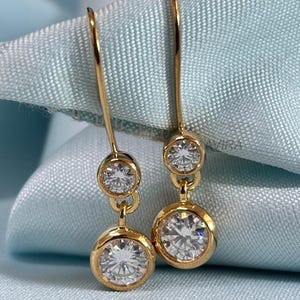 May include: A pair of gold drop earrings with two round clear stones. The earrings have a simple design and are perfect for everyday wear.