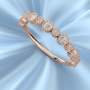 May include: Rose gold ring featuring a series of small, round, clear gemstones set in a beaded bezel design. The ring has a delicate, curved band and is displayed against a light blue background.