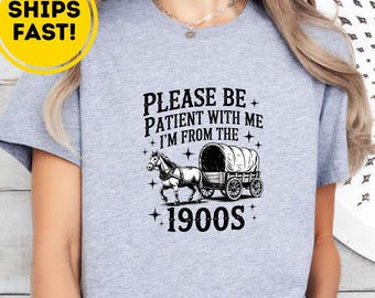 Puede incluir: Camiseta gris jaspeado con el texto "PLEASE BE PATIENT WITH ME I'M FROM THE 1900S" y un gráfico de un carro cubierto tirado por caballos. La camiseta también tiene un círculo amarillo que dice "SHIPS FAST!"