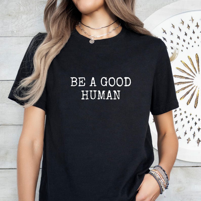 May include: Black t-shirt with the white text "BE A GOOD HUMAN". The shirt is a crew neck style and appears to be made of a soft material. The image shows the shirt on a person.
