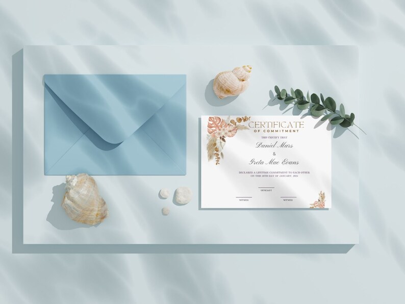 K&ouml;nnte beinhalten: Eine Verpflichtungsurkunde mit den Namen Daniel Mars und Greta Mae Evans, mit floralen Akzenten, liegt neben einem blauen Umschlag, Muscheln und kleinen wei&szlig;en Steinen. Die Urkunde liegt auf einer hellblauen Oberfl&auml;che.