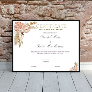 K&ouml;nnte beinhalten: Gerahmte Urkunde mit dem Text &bdquo;Certificate of Commitment&ldquo; und den Namen Daniel Mars und Greta Mae Evans. Die Urkunde ist mit Aquarell-Blumenelementen in Pfirsich-, Beige- und Braunt&ouml;nen verziert.