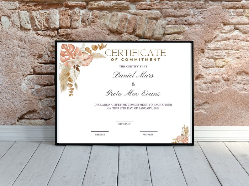 K&ouml;nnte beinhalten: Gerahmte Urkunde mit dem Text &bdquo;Certificate of Commitment&ldquo; und den Namen Daniel Mars und Greta Mae Evans. Die Urkunde ist mit Aquarell-Blumenelementen in Pfirsich-, Beige- und Braunt&ouml;nen verziert.
