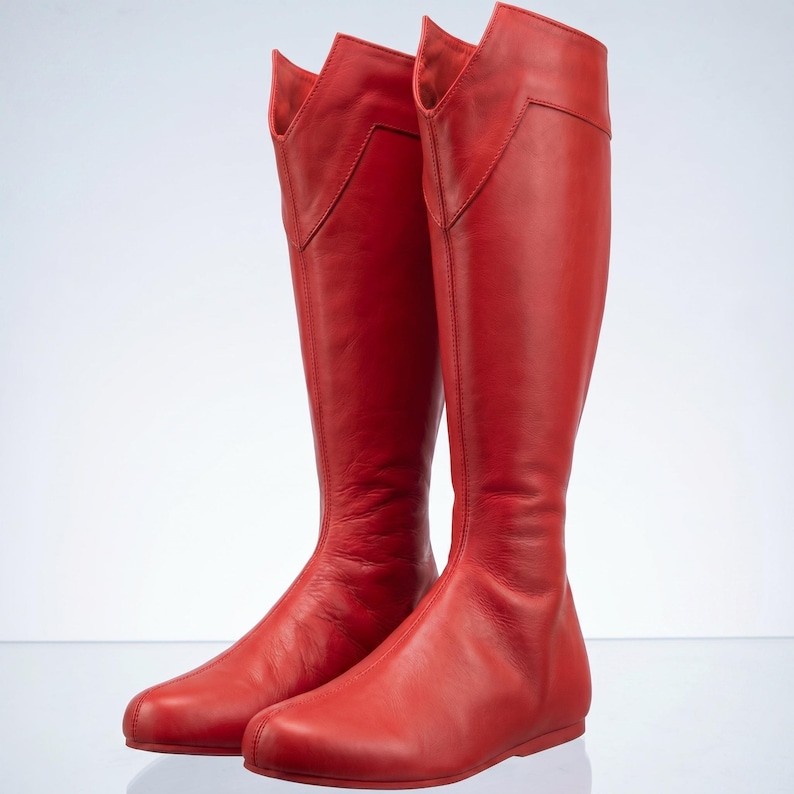 K&ouml;nnte beinhalten: Ein Paar kniehohe rote Stiefel. Die Stiefel haben eine glatte, matte Oberfl&auml;che und ein einzigartiges Design am oberen Schaft. Die Stiefel haben eine flache Sohle und eine stromlinienf&ouml;rmige Silhouette, perfekt f&uuml;r ein mutiges Mode-Statement.