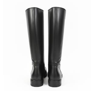 May include: A pair of knee-high black boots with a smooth finish, featuring a structured shaft, a rounded toe, and a low block heel. The boots are shown from the back view, displaying vertical seam detailing along the center of the shaft.