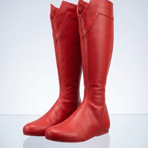 K&ouml;nnte beinhalten: Ein Paar hohe, rote Lederstiefel. Die Stiefel haben ein kniehohes Design mit spitzer Zehenpartie und einem einzigartigen, eckigen Oberteil. Die Stiefel sind aus glattem, gl&auml;nzendem Leder und vor wei&szlig;em Hintergrund.