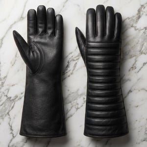 May include: Two black leather gloves, one with a smooth finish and the other with horizontal stitched detailing. The gloves are long, extending past the wrist, and are displayed on a white and gray marble surface.