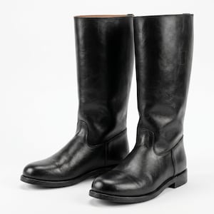 May include: A pair of tall black leather boots featuring a smooth finish, a rounded toe, and a low heel. The boots have a structured shaft that reaches mid-calf, a clean silhouette, and a visible brown interior lining at the top edge of the shaft.