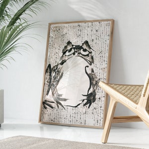 May include: A black and white ink drawing of a frog on a white background with black text. The frog is looking up and has a large belly. The text is in Japanese.