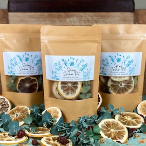 Könnte beinhalten: Drei braune Papiertüten gefüllt mit getrockneten Zitrusfrüchten, Eukalyptusblättern und Lavendel. Die Beutel haben ein weißes Etikett mit dem Text "Spring Summer Pot" und einem floralen Design.