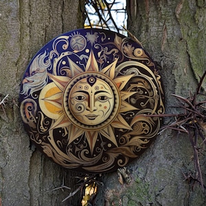 Puede incluir: Una placa redonda de madera decorativa con un diseño de sol dorado. El sol tiene una cara humana con un tercer ojo y está rodeado de intrincados patrones florales. La placa está montada en un tronco de árbol con espinas.
