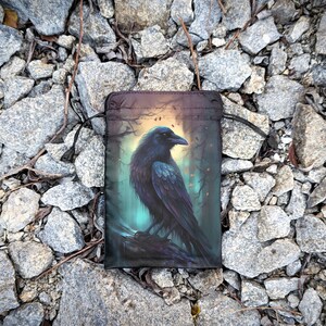 May include: A black drawstring bag with a raven illustration. The raven is perched on a branch in a dark forest setting with a glowing light behind it.