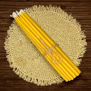 May include: A bundle of yellow beeswax candles tied together with twine, resting on a natural woven straw placemat.