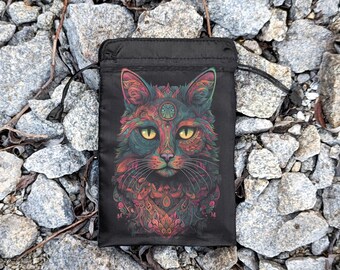 Puede incluir: Una bolsa negra de cordón con un diseño de gato psicodélico colorido. Los ojos del gato son verdes y su pelaje es una mezcla de rojo, naranja, amarillo, verde, azul y morado.