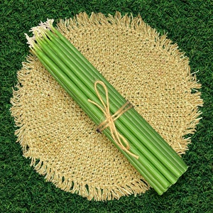 May include: A bundle of green candles tied together with twine, resting on a round, beige crocheted placemat. The placemat has a fringe border and is set against a green grassy background.