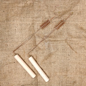 May include: Two wooden handled metal skewers with a spiral design. The skewers are on a brown burlap background.