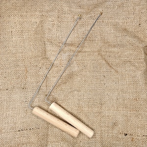 May include: Two wooden handled metal skewers with gold tips. The skewers are lying on a brown burlap surface.