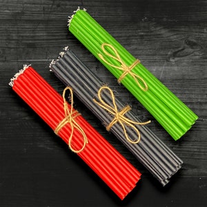 May include: Three bundles of candles, tied with twine, in red, black, and green. The candles are arranged on a black wooden surface.
