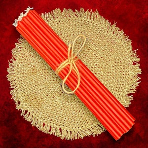 May include: A bundle of red taper candles tied together with twine, resting on a beige crocheted doily.