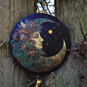 May include: A round wooden wall hanging with a crescent moon design. The moon is decorated with intricate floral patterns and a stylized face. The background is a dark blue with gold stars.
