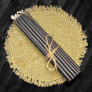 May include: A bundle of black candles tied together with twine, resting on a gold crocheted placemat.