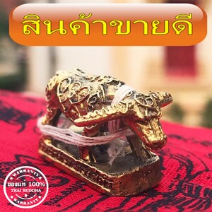 May include: A small golden statue of a buffalo, with intricate details, sitting on a red and gold patterned surface. The statue is tied with a white string. The text "สินค้าขายดี" is visible in the background.