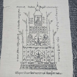 May include: A cream-colored fabric with a detailed black ink drawing of a temple-like structure. The design includes multiple levels, figures of seated Buddhas, and intricate patterns. Text in a foreign script surrounds the central image.