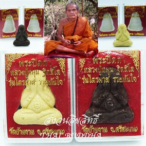 May include: Two small, hand-crafted, Buddha statues in a seated position with hands clasped in front of their faces. One statue is white and the other is black. Both statues are in protective cases with red and gold trim. The text on the cases reads "พระปิดตา หลวงปู่หมุน ฐิตสีโล รุ่นไตรมาสรวยทันใจ" which translates to "Buddha Amulet, Luang Pu Mun, Trimas, Wealthy, Quick".