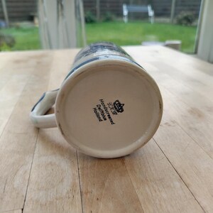 May include: A ceramic beer stein with a blue and white floral design. The stein has a handle and the text "Handscreened Delftblue Holland" is visible on the bottom. The stein is made of ceramic.