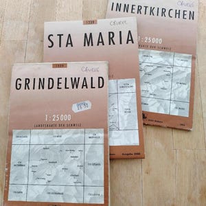 May include: Three vintage Swiss topographic maps. The maps are titled "Grindelwald", "Sta Maria", and "Innertkirchen". Each map has a brown and white color scheme with detailed geographical information and the scale 1:25000.
