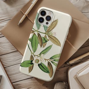 Könnte beinhalten: Eine cremefarbene Handyhülle mit einer botanischen Illustration von grünen Blättern, braunen Stielen und weißen Blüten. Die Hülle liegt auf einer Holzoberfläche mit Schreibwaren.