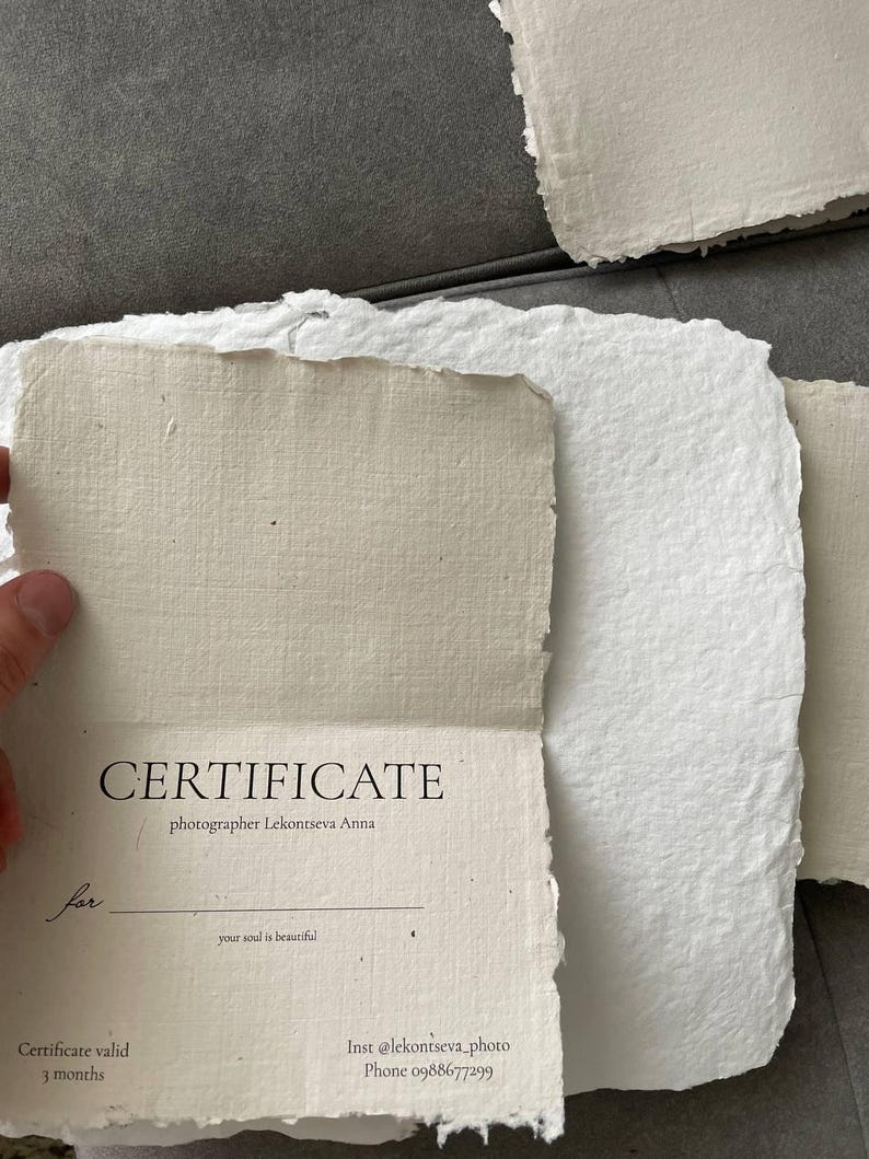 May include: A stack of handmade paper sheets, some with deckled edges, in shades of white and beige. One sheet is open, revealing the word "CERTIFICATE" and the photographer's name. The text includes "Certificate valid 3 months".