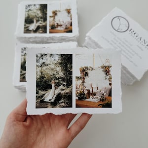 Puede incluir: Una mano sostiene una impresión fotográfica con bordes irregulares que muestra dos escenas de boda. La impresión muestra a una novia en un bosque y un área de recepción decorada. Una pila de impresiones similares y tarjetas de visita en el fondo.
