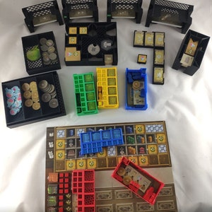 Könnte beinhalten: Ein Spielbrett mit verschiedenen farbigen Kunststoffbehältern und Tabletts. Das Brett ist braun mit einem Gittermuster und goldenen Akzenten. Die Behälter sind blau, rot, grün und gelb. Die Tabletts sind schwarz und enthalten kleine Münzen und Spielsteine.