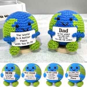 Puede incluir: Muñecos de peluche con forma de Tierra, tejidos a ganchillo en azul y verde, cada uno con un cartel. Uno dice "The World Is A Better Place With You In It!", otro dice "Dad". Otros carteles dicen "Mom", "Best Friend", "To My Love" y "You Make The World a More Awesome Place".
