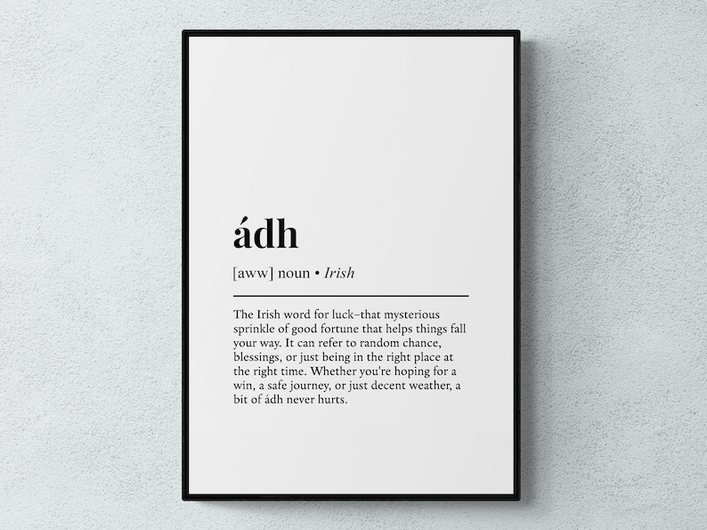 Op de afbeelding: Een ingelijste print met het Ierse woord "&aacute;dh", wat geluk betekent, in zwarte letters op een witte achtergrond. De tekst wordt omlijst door een zwarte lijst. Geschikt voor interieurdecoratie.