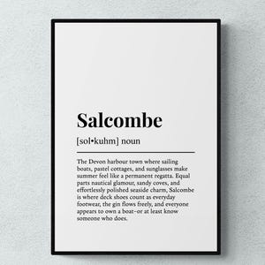 May include: A framed wall art print featuring a dictionary-style definition of Salcombe. The text includes the phonetic pronunciation, the noun classification, and a descriptive paragraph about the Devon harbour town, all in black ink on a white background.