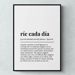 May include: A rectangular wall art print in a black frame featuring the Spanish phrase ríe cada día in bold black text. Below the phrase is a phonetic pronunciation guide and a paragraph of English text explaining the meaning of the phrase.