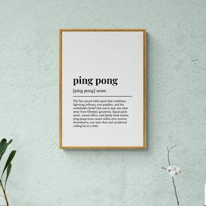 Puede incluir: Un cartel enmarcado con las palabras "ping pong" en negrita. La definici&oacute;n de ping pong est&aacute; debajo del t&iacute;tulo. El marco es dorado y el fondo es blanco. El cartel est&aacute; colgado en una pared verde claro.