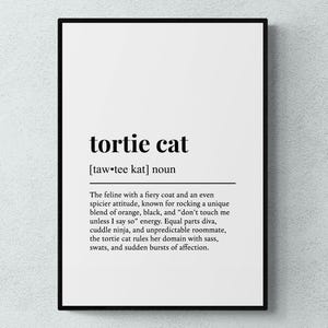 May include: A framed print with the definition of "tortie cat" in black text on a white background. The definition includes the pronunciation and a description of the cat's personality, including its fiery coat and sassy attitude.