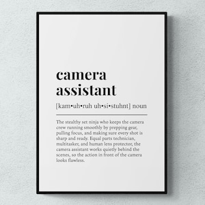 May include: A framed print featuring the words "camera assistant" in black, bold font. The phonetic pronunciation is below. A definition of the role is also provided in black text.