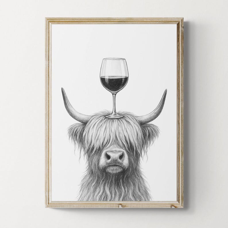 May include: Framed black and white print of a Highland cow with a wine glass balanced on its head. The cow has long, shaggy fur and curved horns. The wine glass is filled with red wine.