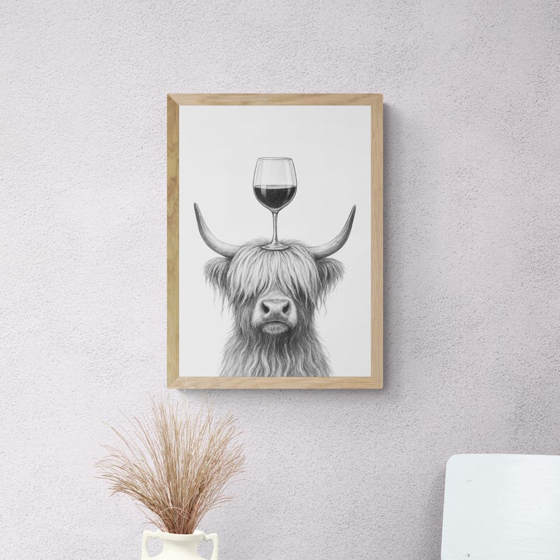May include: Framed black and white print of a Highland cow with a wine glass balanced on its head. The artwork features a detailed pencil drawing style, with the cow's shaggy fur and horns clearly visible. The wine glass is filled with red wine.