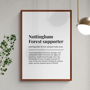 May include: A framed print with the text "Nottingham Forest supporter" in black font. The print includes a definition and description of a supporter. The frame is brown, and the background is white.