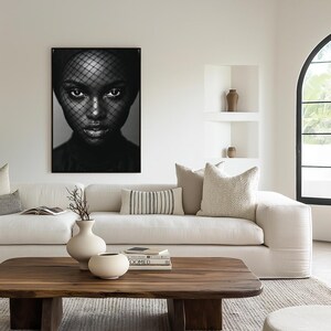 Può includere: Un ritratto in bianco e nero di una persona con un velo, incorniciato e appeso a una parete bianca. La stanza presenta un divano bianco con cuscini decorativi, un tavolino in legno e vasi decorativi. Tema: design d'interni moderno.