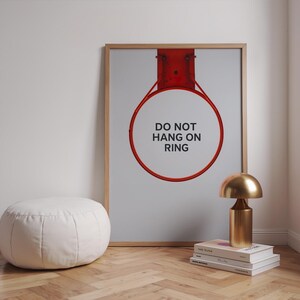 Könnte beinhalten: Gerahmter Druck mit rotem Basketballkorb und dem Text "DO NOT HANG ON RING". Eine goldfarbene Lampe steht auf Büchern. Links befindet sich ein weißer, runder Hocker.